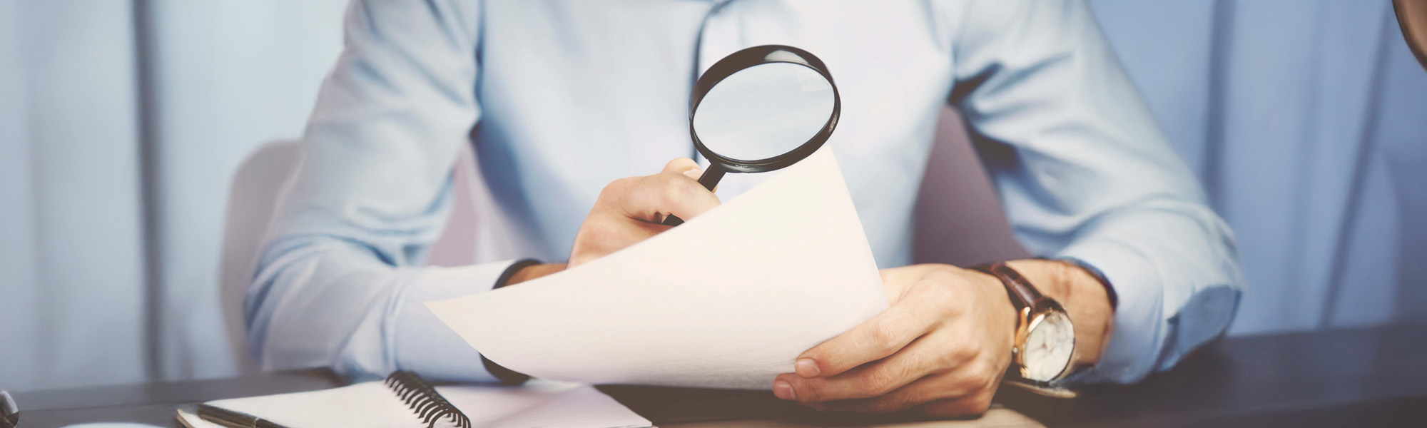 man using magnifying glass to look at documents