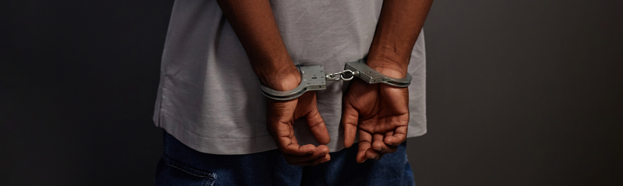 Black man arrested standing by wall with handcuffs